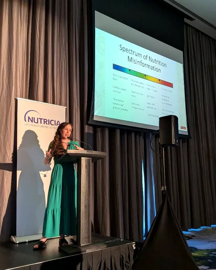 Maeve Hanan speaking at a lectern on stage, with a slide titled “Spectrum of Nutrition Misinformation” behind her
