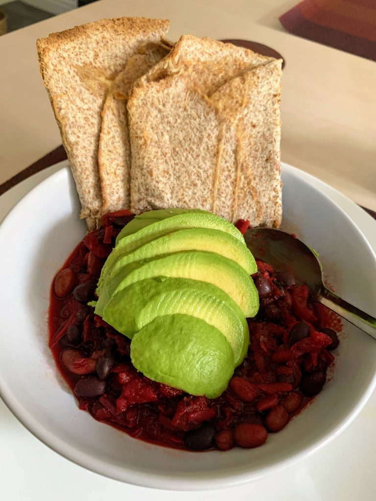 A white bowl filled with purple beetroot chilli, topped with sliced avocado and 2 toasted cheesy wraps.